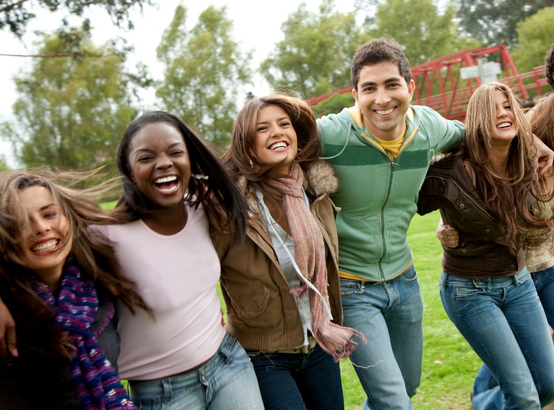 Group of friends laughing with each other outside. There are four girls and one boy and there is a red bridge behind them.