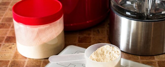 A measuring cup with pre-workout powder. There are jars with red lids and a weight scale.
