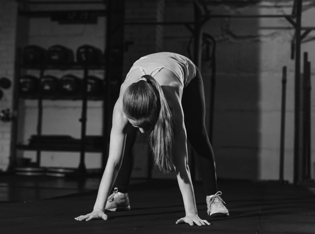 There is a woman in a black and white photo who is stretching downward with her hands and feet on the ground.